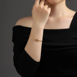 Close-up of minimalist gold heart knot bangle on wrist with a high-polished finish