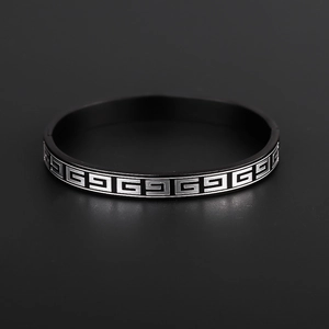 Detail of matte black titanium steel ring with silver Greek key pattern on dark background