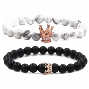 Detalle de pulseras de ónix negro mate y turquesa blanca con coronas en oro rosa
