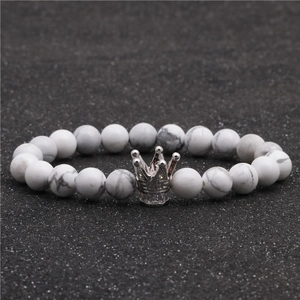 Detalle de pulsera de cuentas de turquesa blanca con amuleto de corona sobre arena negra