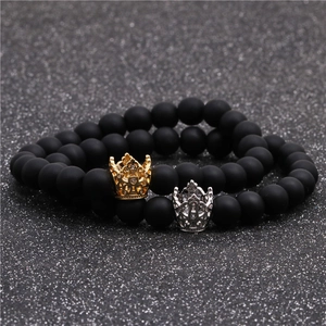 Vista macro di braccialetti con corona e perle nere opache in finiture oro e argento