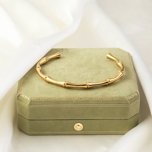 Detail view of a golden bamboo-shaped open bangle on a green velvet jewelry box