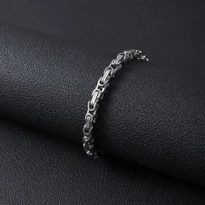 Detail shot of a silver Byzantine chain bracelet on a black textured display stand