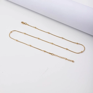 Detail van een gouden roestvrijstalen slangenketting met kleine kralen en een karabijnsluiting