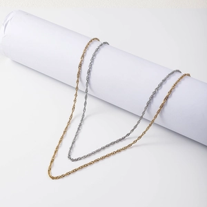 Close-up of gold and silver water wave chain necklaces draped over white paper rolls