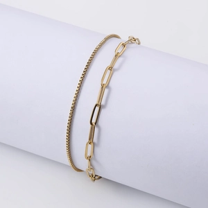 Double-layered gold paperclip and box chain bracelet displayed on a white stand