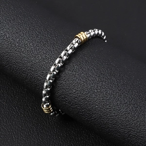 Polished stainless steel box chain bracelet with gold bead accents on a black display stand