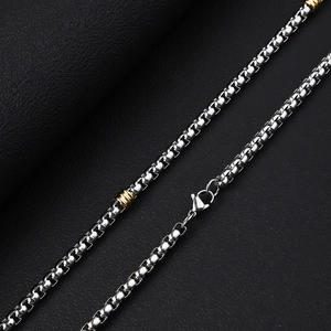 Macro shot of stainless steel box chain necklace with gold cylinder beads on black leather
