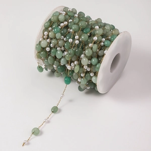 Detail of DIY jewelry chain with green jade beads and pearls on a white plastic spool