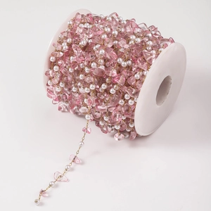 Detail view of DIY handmade chain with pink resin stones and white pearls on spool