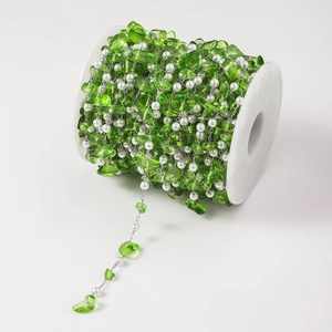 Detailed macro view of green resin stone and white pearl beads on a silver DIY chain