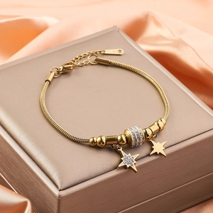 Detail of 18K gold snake chain bracelet with sparkling crystal star charms on satin