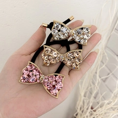 Close-up of three crystal bow hair ties in pink, champagne, and clear on black elastic bands