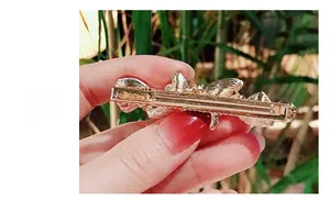 Close-up of golden metal hair clip featuring a classic duckbill structure and embossed detail