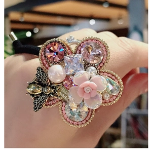 Detailed close-up of hair tie with pink resin rose, crystal flower, and gold bee charm