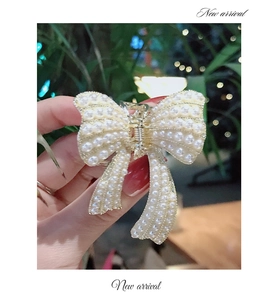 Dettaglio di un fermaglio per capelli dorato a fiocco decorato con perle bianche