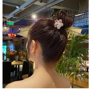 Detail of pink crystal flower hair tie with pearl center worn on a bun hairstyle