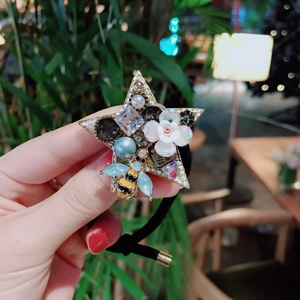 Macro shot of starry hair tie with white flowers, blue pearls, and a crystal bee ornament