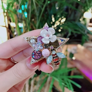 Detail of star-shaped hair tie featuring white flowers, pearls, and a tiny bee accent