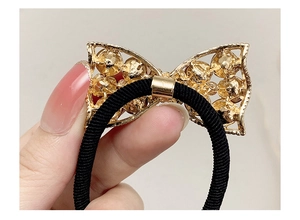 Detail view of rhinestone bow hair tie with golden frame and elastic black band