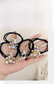 Hand holding four crystal bear hair ties in blue, purple, red, and champagne colors