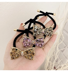 Three rhinestone bow hair ties in champagne gold, pink, and grey held in hand