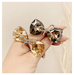 Detailed macro view of champagne and smoky grey crystal bow hair accessories held in hand
