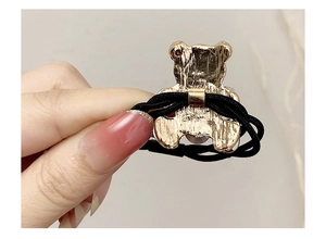 Detail of the golden metal bear charm and secure elastic band attachment on the hair tie