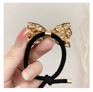 Close-up of a high-elastic black hair tie featuring a golden metallic bow with textured details