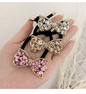 Close-up of three elastic hair ties with rhinestone bows in pink, white, and champagne gold