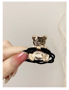 Close-up of golden bear charm showing metal texture and elastic hair tie detail