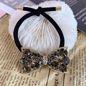 Elegant bow hair tie with grey crystals and gold metal finish on vintage newspaper