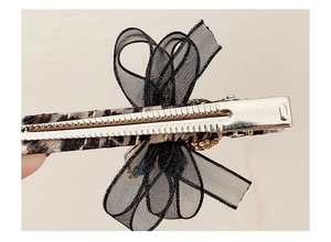 Macro view of leopard print hair clip with black organza bow and sparkling rhinestones