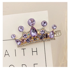 Dettaglio del fermaglio a corona dorata con strass, cristalli viola e medaglietta