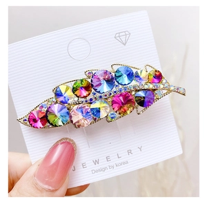 Detailed view of leaf-shaped hair clip with colorful crystals on a gold alloy base
