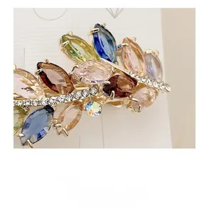 Macro detail of leaf-shaped hair clip with colorful gemstones and white rhinestones