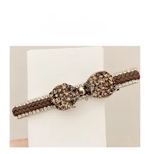 Détail d'une pince à cheveux tressée marron avec des strass champagne sur carte blanche
