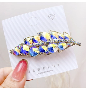 Close-up of leaf-shaped hair clip with vibrant gradient crystals and golden metal veins