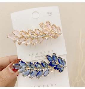 Detail of leaf-shaped hair clips with pink and blue crystals on golden metal base