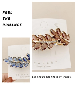 Detail of leaf-shaped crystal hair clips in grey and blue with golden metal base