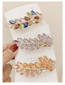 Detailed view of three leaf-shaped spring hair clips with colorful crystals and rhinestones