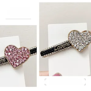 Detailed macro view of heart shaped rhinestone hair clip with golden Loveme letters on black base