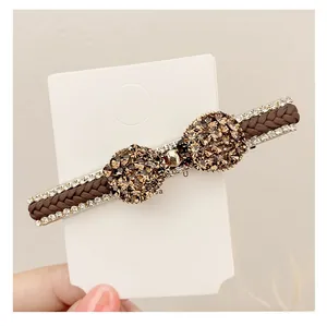 Détail d'une pince à cheveux nœud en cuir tressé marron foncé et strass champagne
