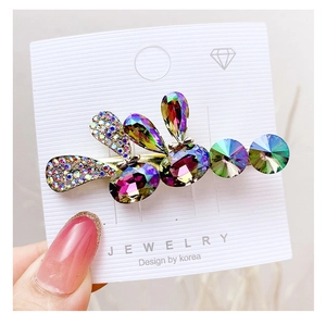 Close-up of a leaf-shaped hair clip with colorful rhinestones on a golden base