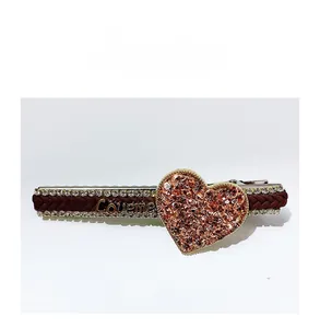 Detail of rhinestone heart hair clip with woven brown ribbon and Loveme gold lettering