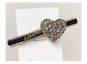 Detailed view of woven black hair clip featuring rhinestone heart and Loveme gold lettering