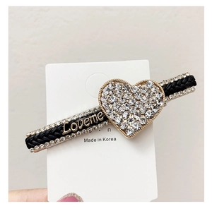 Detail of rhinestone heart hair clip with gold Loveme lettering on a woven black base