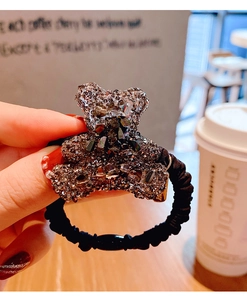 Dettaglio di un ciondolo a forma di orsetto con strass scintillanti su elastico nero per capelli