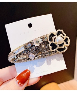 Détail de la barrette en forme de goutte avec fleur de camélia noire et strass brillants