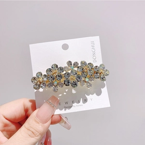 Dettaglio della clip per capelli a fiore dorato con strass grigi su cartoncino